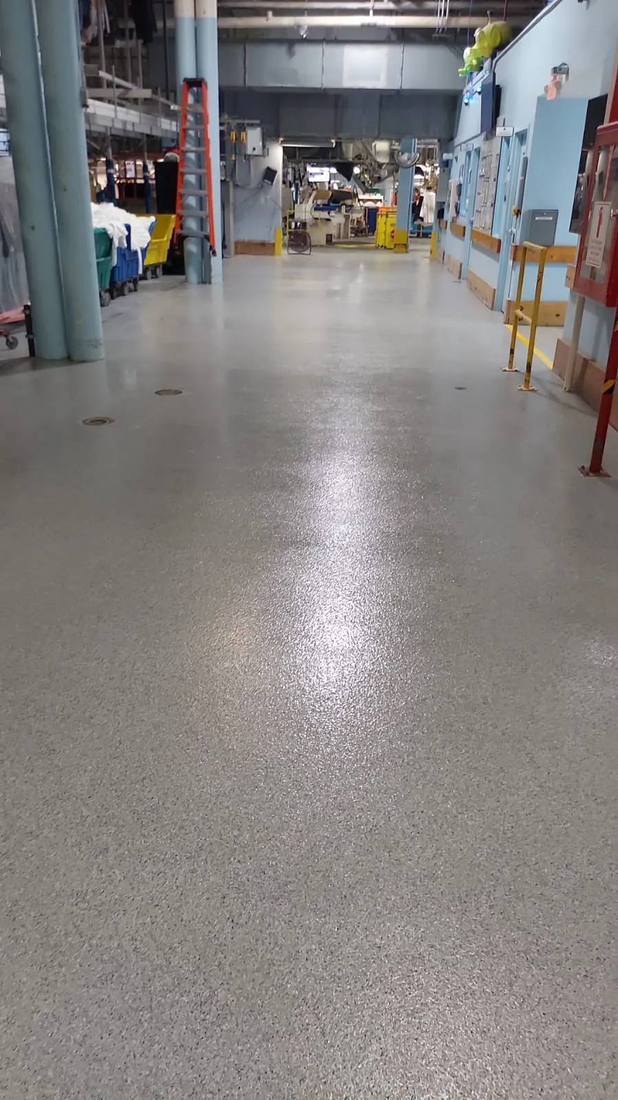 Glossy grey flake-coated aisle in a working industrial facility, with support columns and equipment along both sides