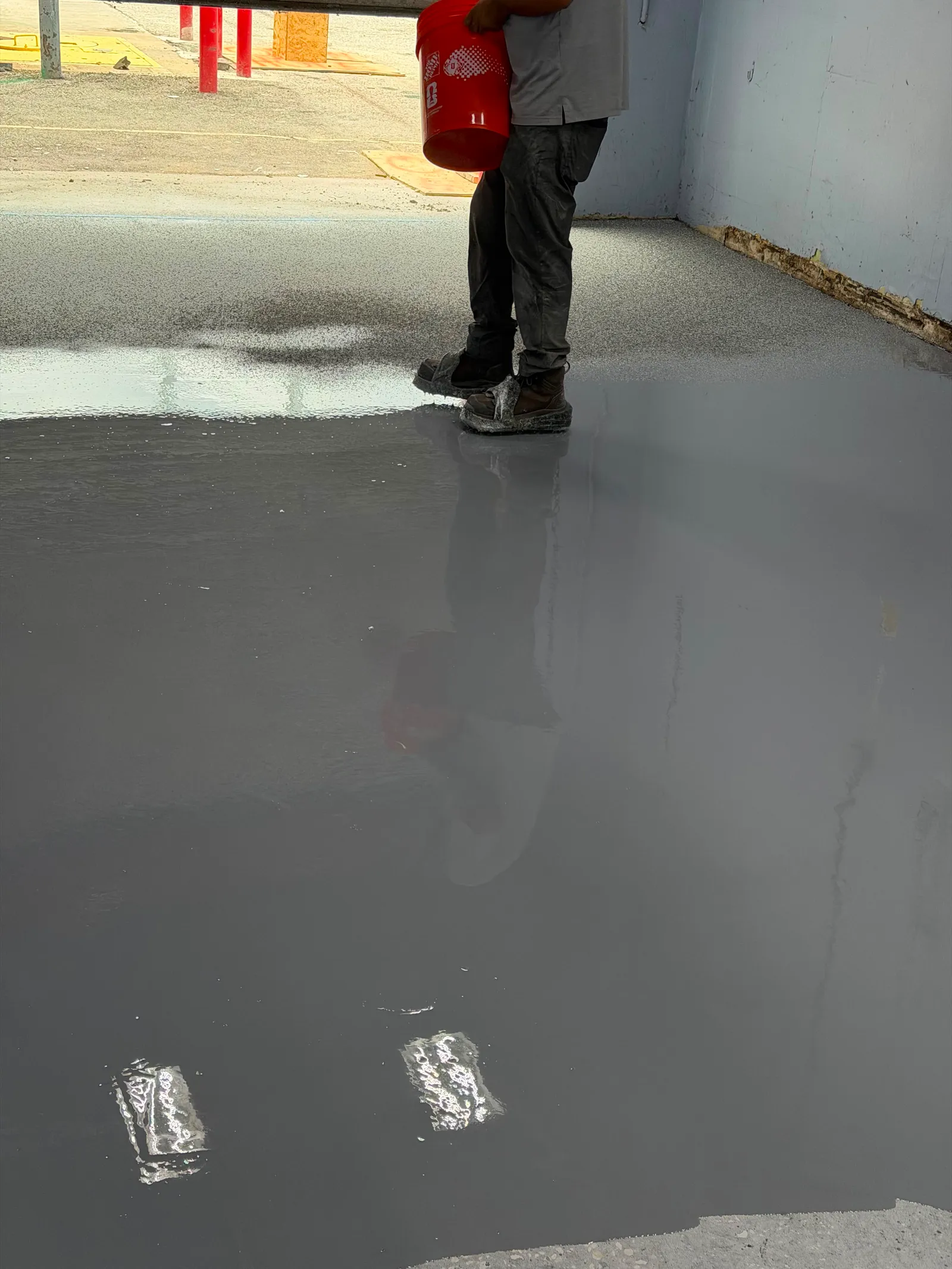 Installer squeegeeing a fresh solid-color base coat across a prepared concrete floor