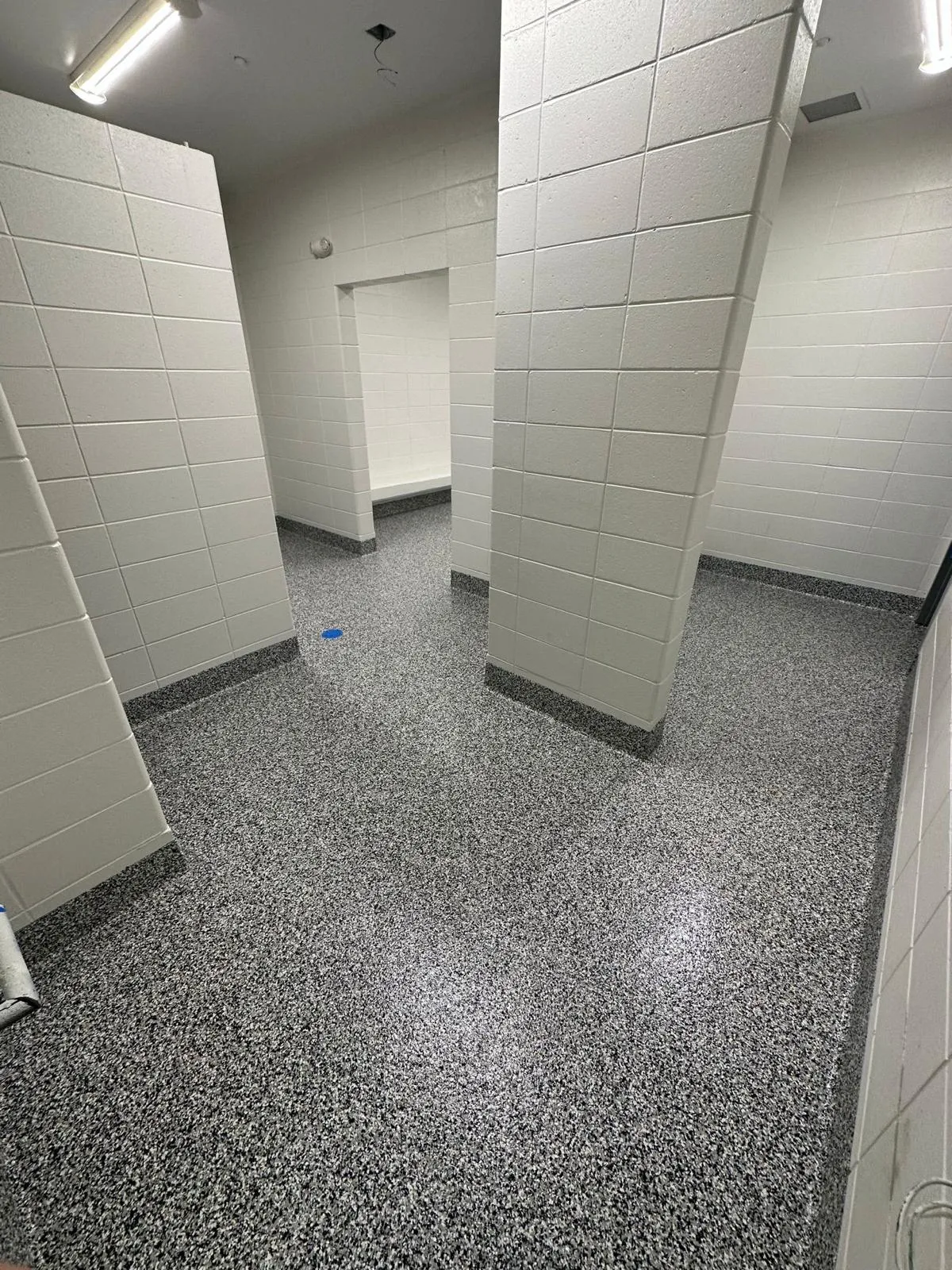 Speckled decorative flake floor in a commercial restroom with block walls and partitions