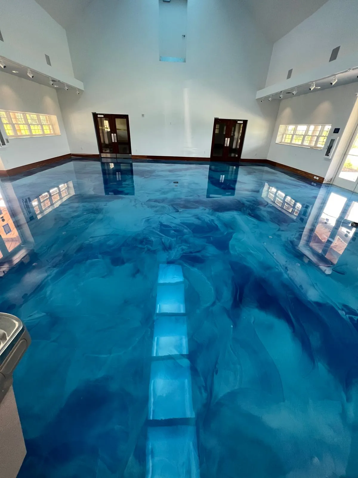 Ocean-blue metallic epoxy floor with swirled depth installed in an indoor residential pool enclosure