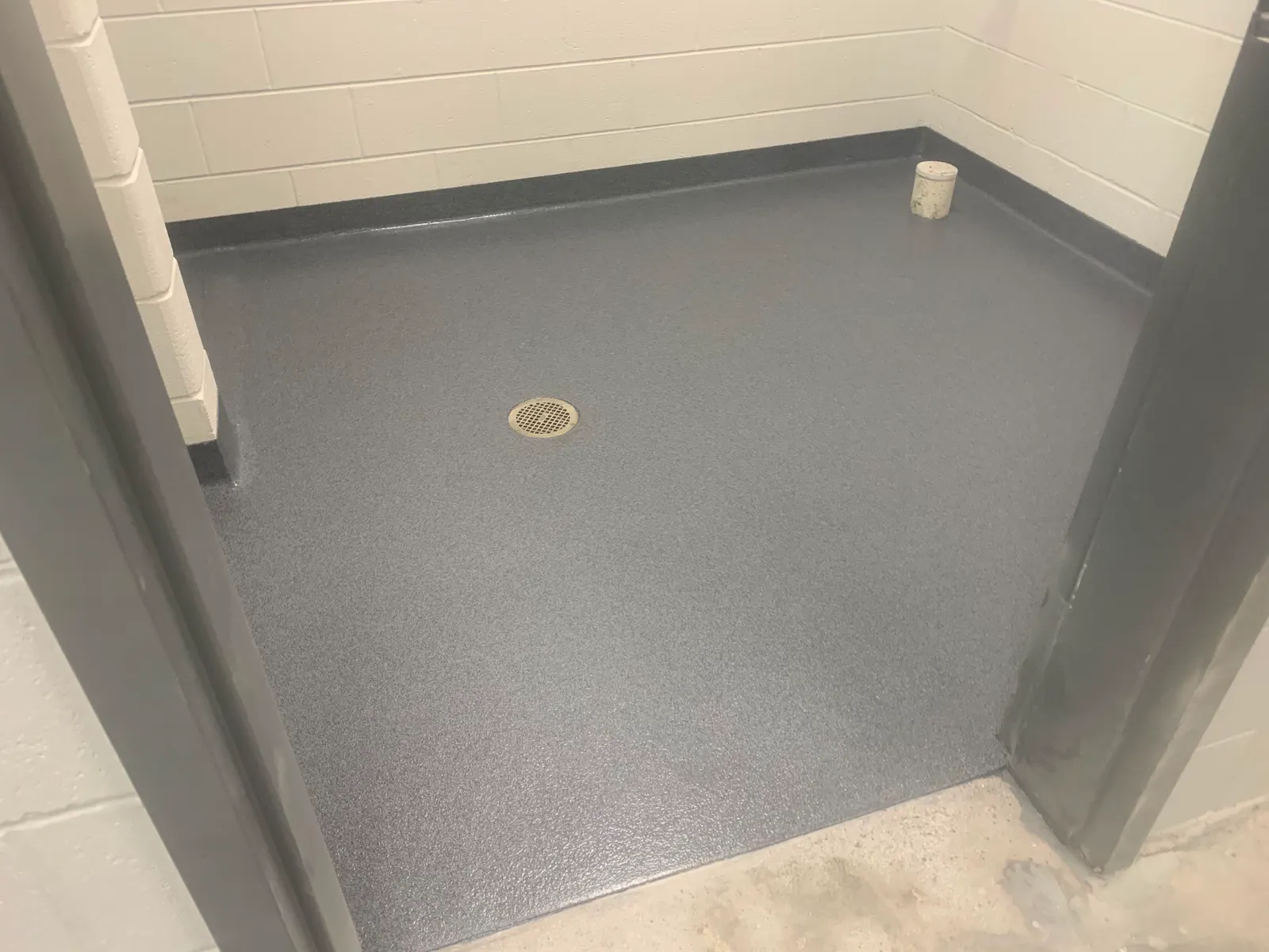 Grey decorative quartz floor with integral cove base and a recessed drain in a restroom