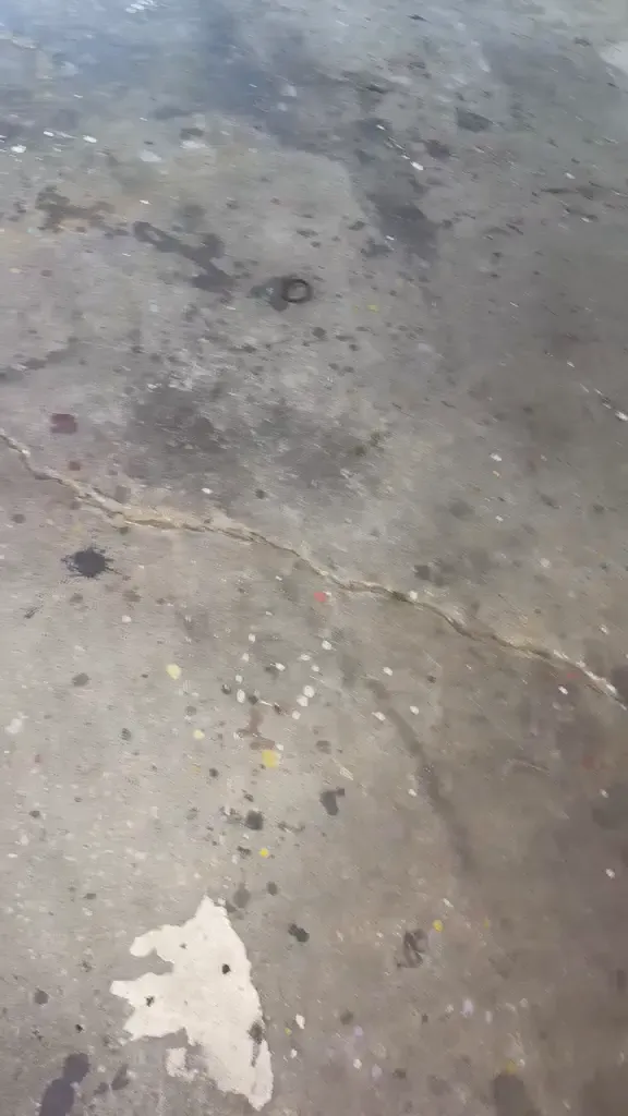 Close view of the bare garage slab before coating, showing a long crack running across the concrete with old paint and oil staining.