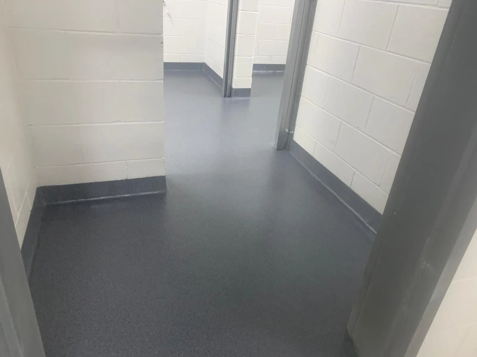Grey urethane floor with dark cove base running through a block-wall corridor