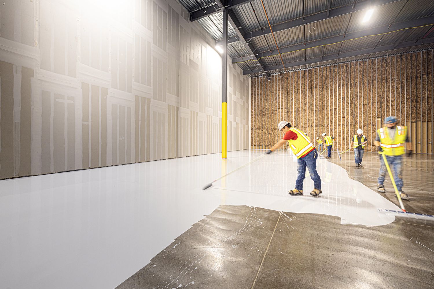 Installers applying a fresh floor coating across a prepared concrete slab